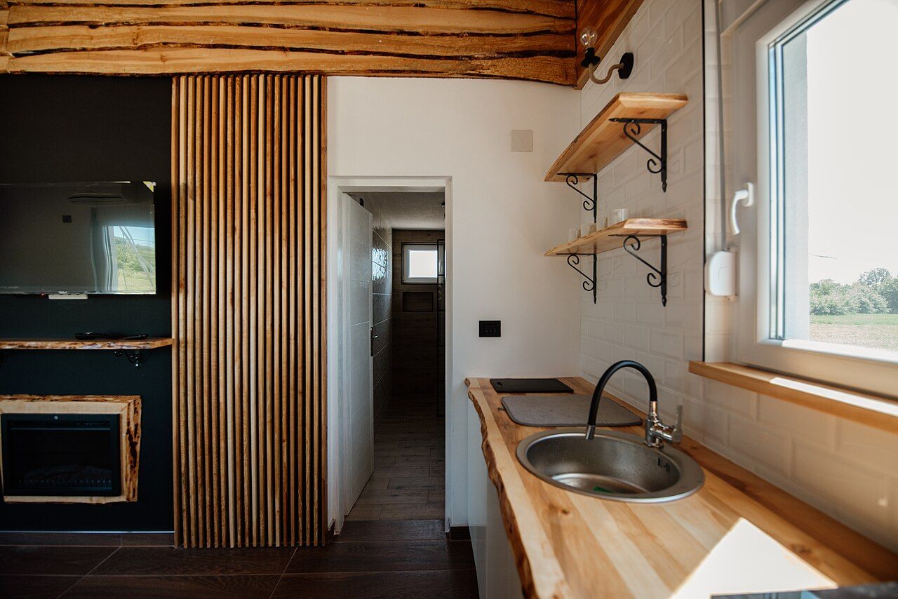 Cocina pequeña con encimera de madera maciza, estantes con escuadras negras y un panel de lamas verticales junto a una ventana.